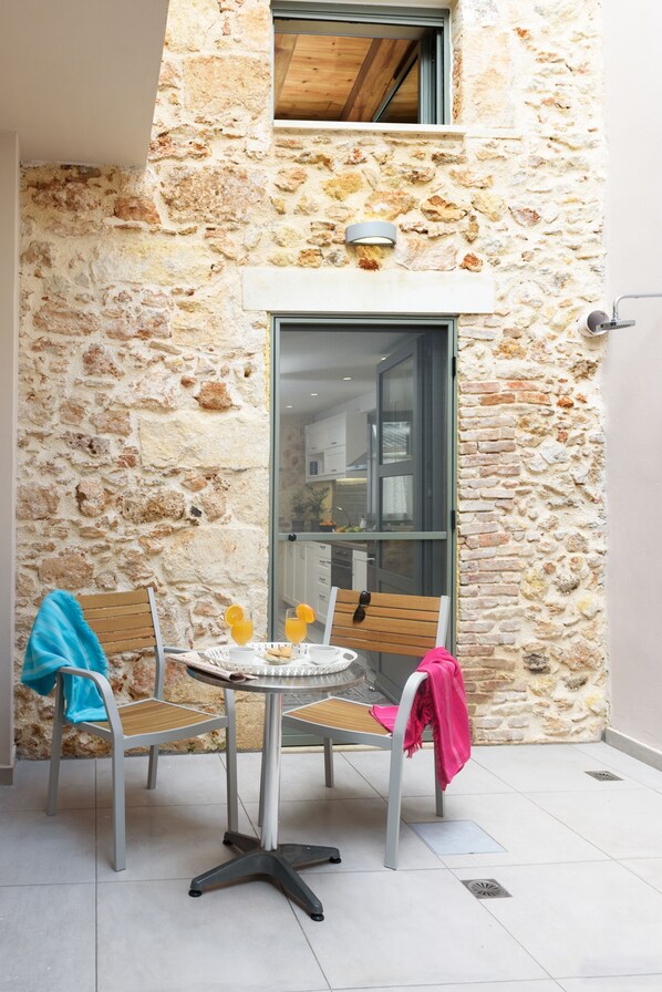A stone-walled outdoor seating area with two chairs and a table, a glass door, and a small window above. - Casa Teresa (Chania)