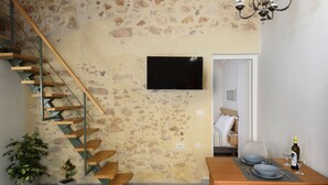 Eine Treppe mit Holzbeschlägen und Metallgeländern, ein Flachbildfernseher an einer strukturierten Wand, ein Esstisch gedeckt mit Tellern und Weingläsern sowie ein Blumentopf.