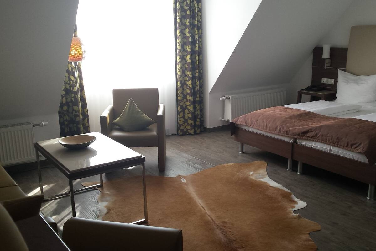 Ett modernt hotellrum med en säng, en stol, ett bord och en matta av kohud.