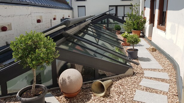 A rooftop terrace with potted plants, a glass awning, and a stone sphere. - Hotel Pfälzer Hof (Edenkoben)