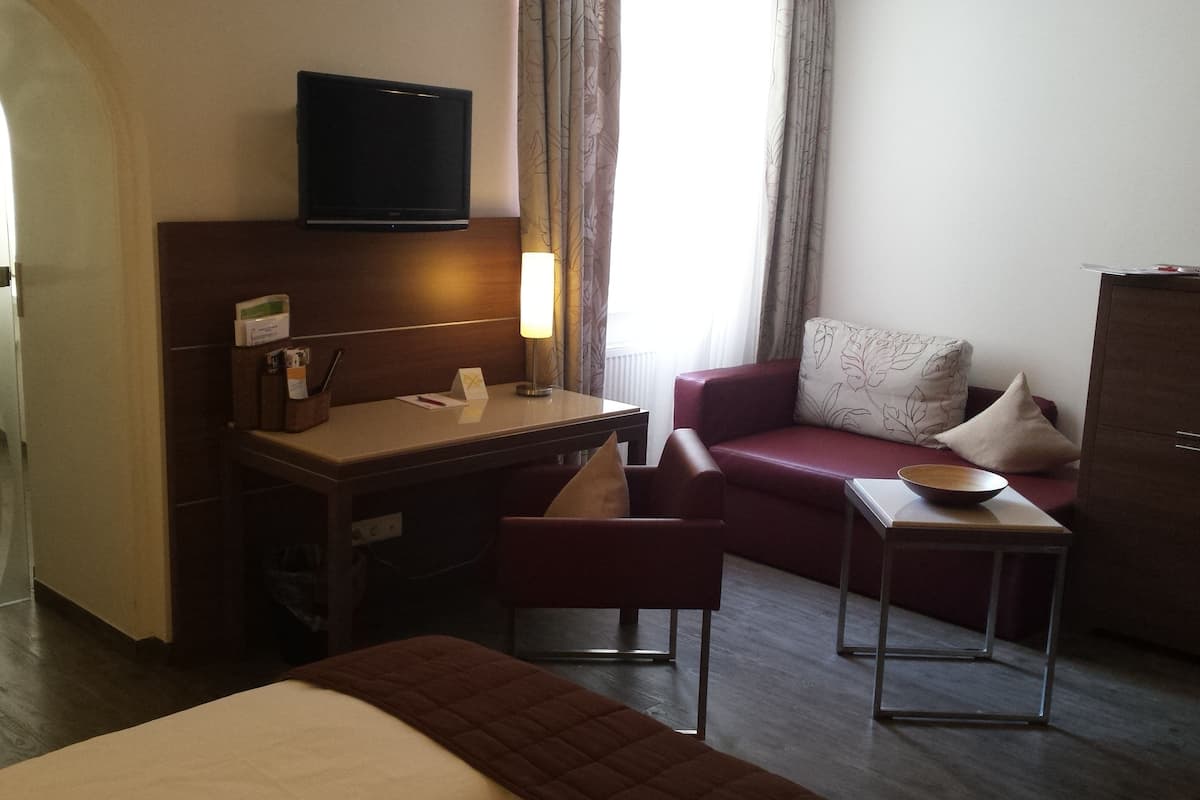 Ett hotellrum med en säng, ett skrivbord, en tv, en soffa och ett litet bord med en skål.
