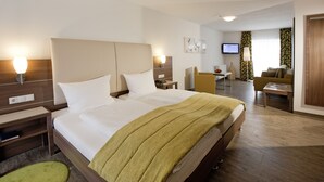 A hotel room with a large bed, bedside tables, a desk, a chair, a television, and a sofa. - Hotel Pfälzer Hof (Edenkoben)