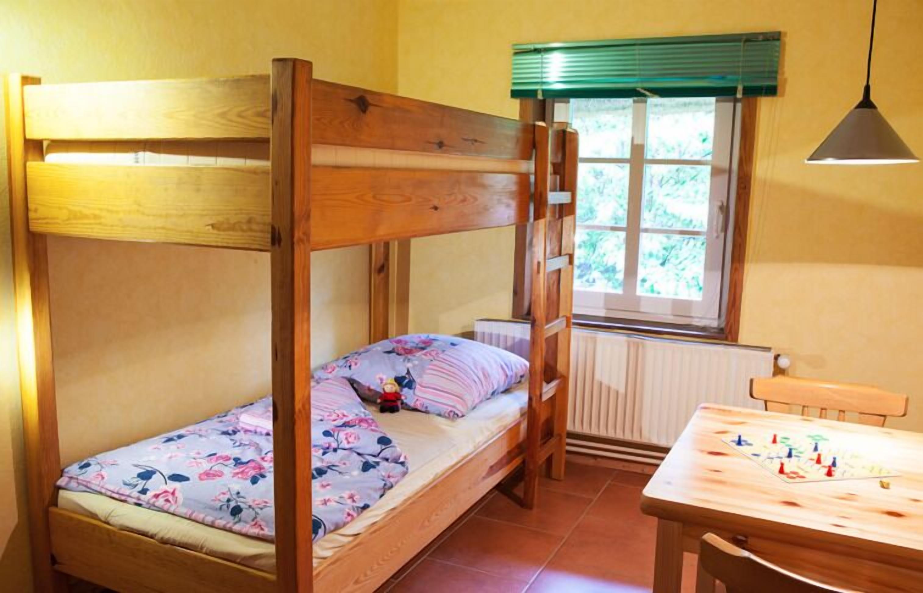 A bunk bed with a floral bedspread, a small table with a board game, and a window with blinds.