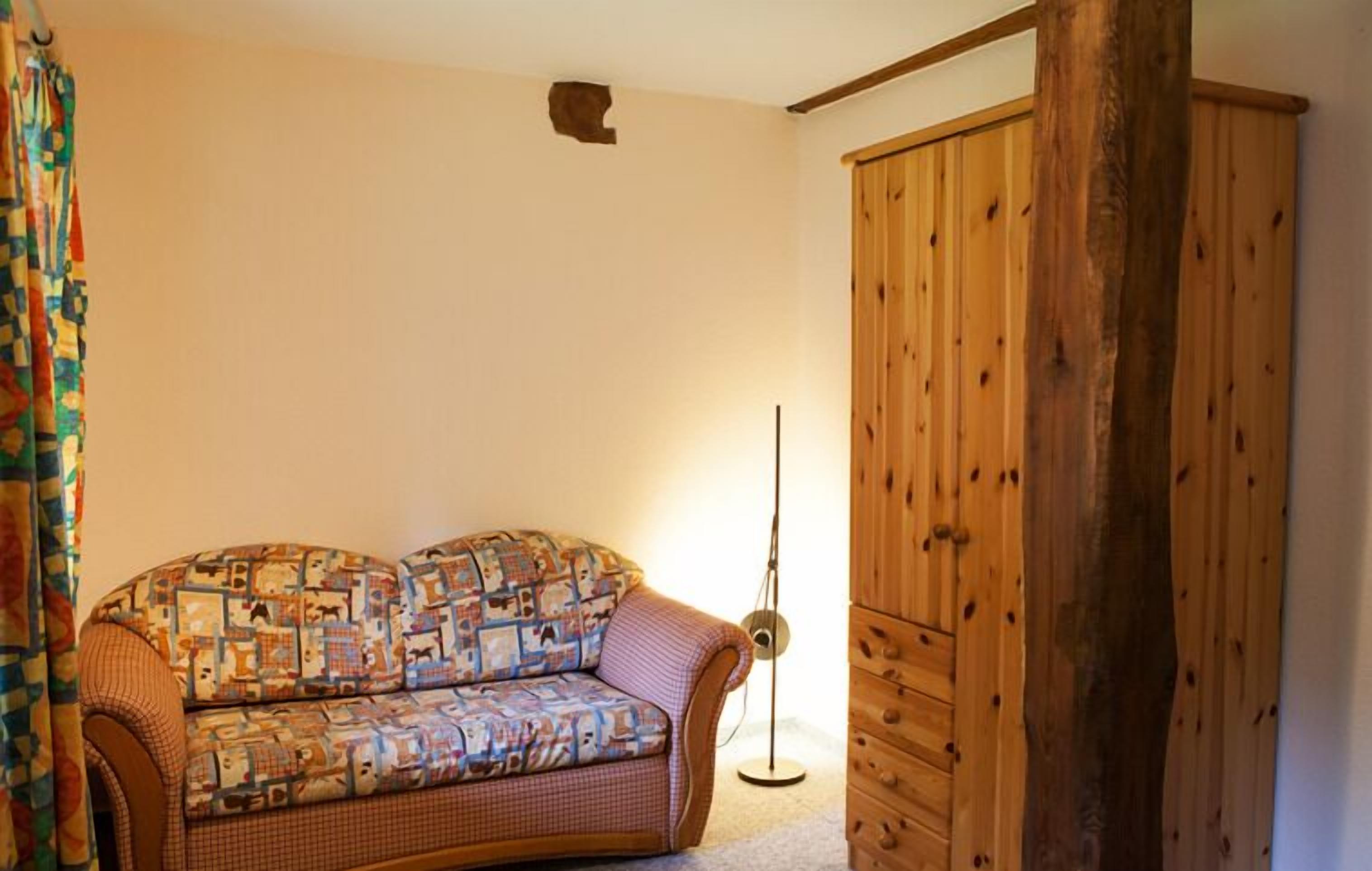 A room with a patterned sofa, a wooden wardrobe, and a floor lamp.