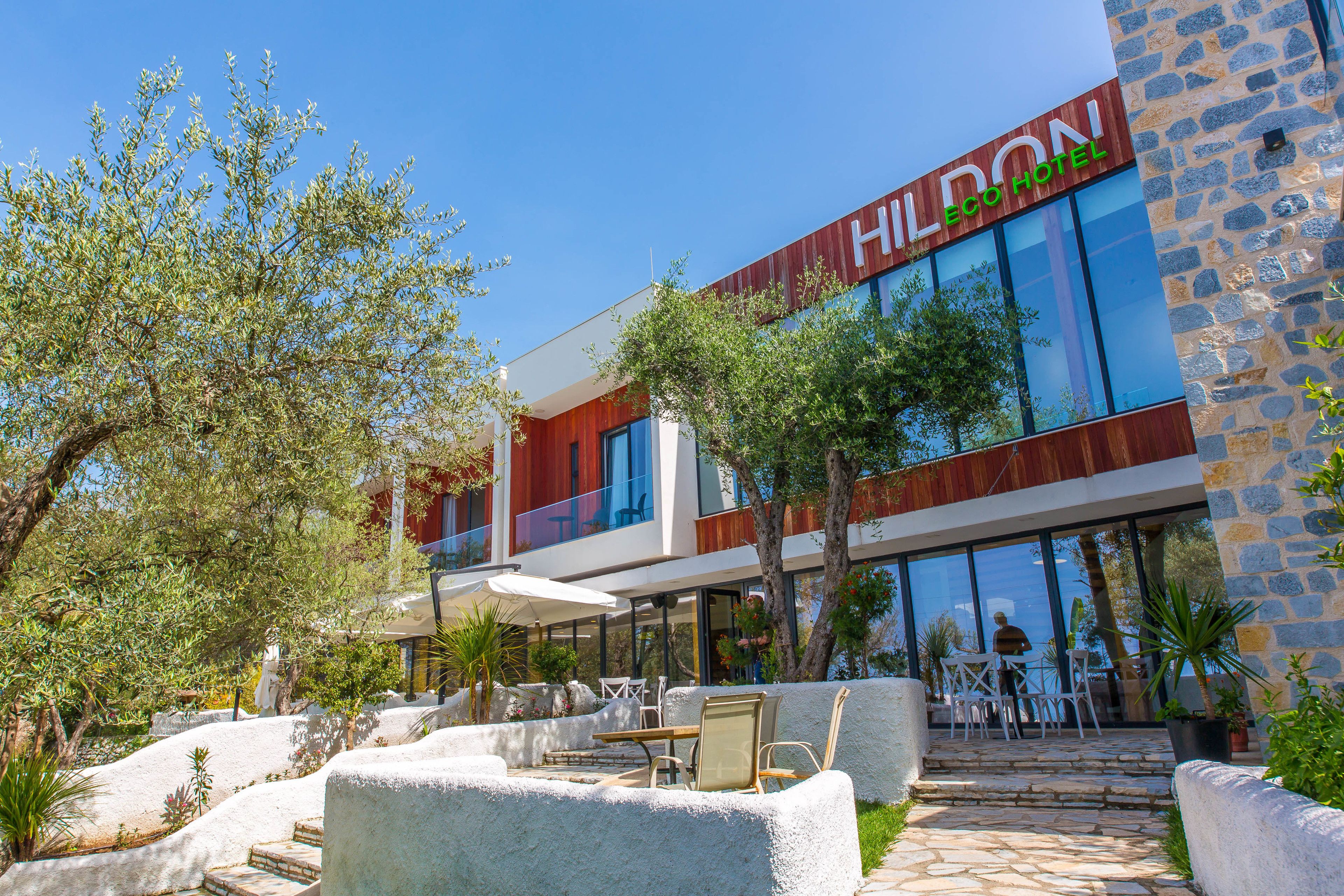 A modern hotel with a stone facade, outdoor seating, and a clear view of the interior through large windows.