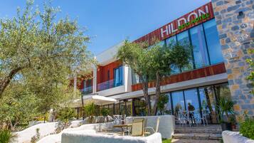 A modern hotel with a stone facade, outdoor seating, and a clear view of the interior through large windows.