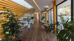 Un interior moderno con una escalera de madera, plantas en macetas y vistas amplias a través de grandes ventanales.