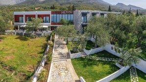 Un hotel moderno con un camino de piedra que conduce a la entrada, rodeado de vegetación y con montañas al fondo.