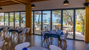 Un restaurante con mesas y sillas dispuestas para comer, amplios ventanales que ofrecen vistas al exterior y vigas de madera en el techo.