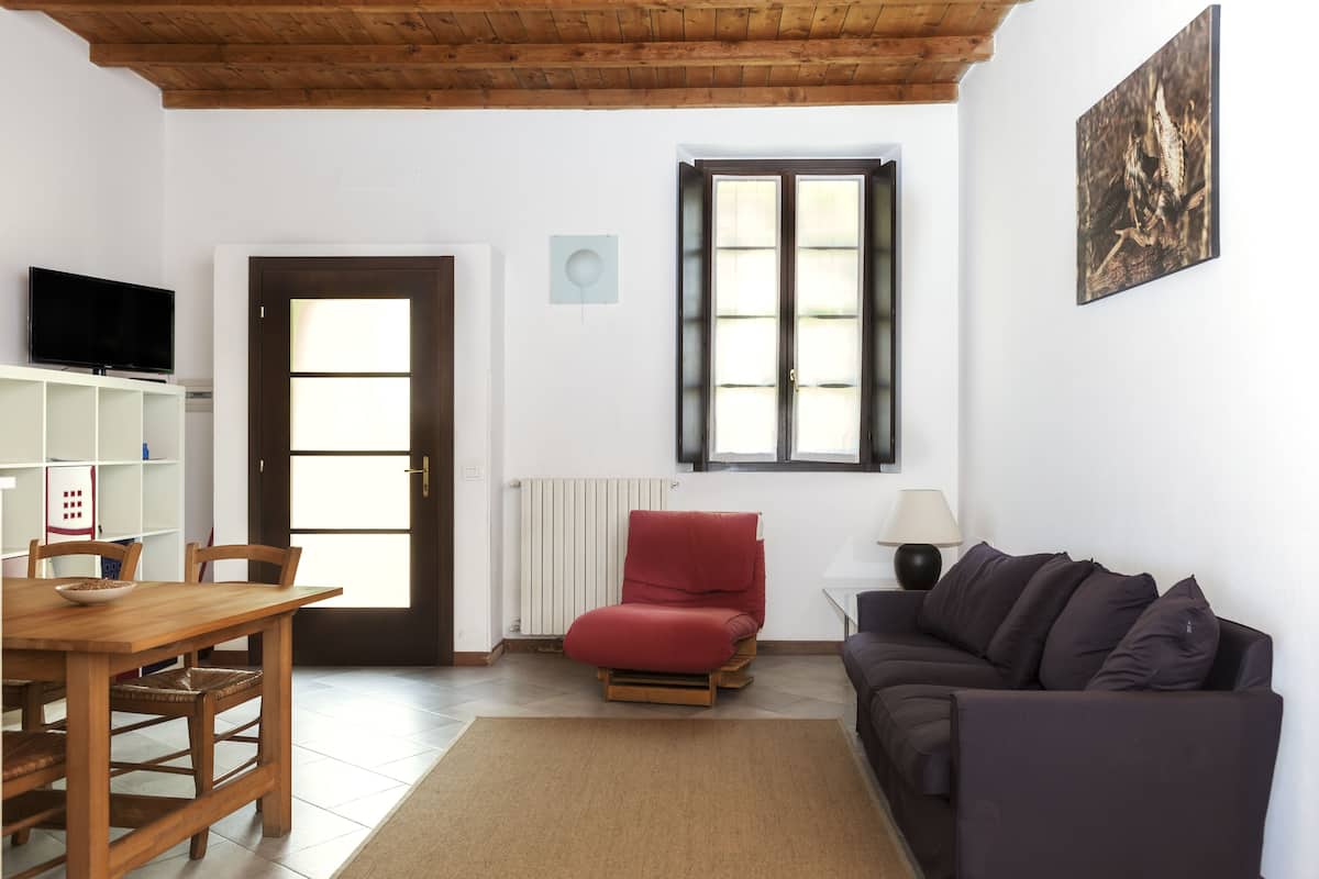 Una sala de estar con una mesa de comedor de madera, una silla roja, un sofá oscuro y una ventana con persianas.