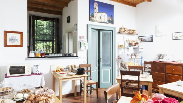 A dining area with a wooden table, chairs, a vase with flowers, and a window with a view of greenery. - Agriturismo Cascina Scanna (Cisliano)