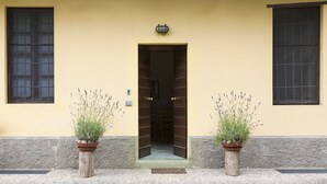A building entrance with a yellow facade, two potted plants, and a door leading inside. - Agriturismo Cascina Scanna (Cisliano)
