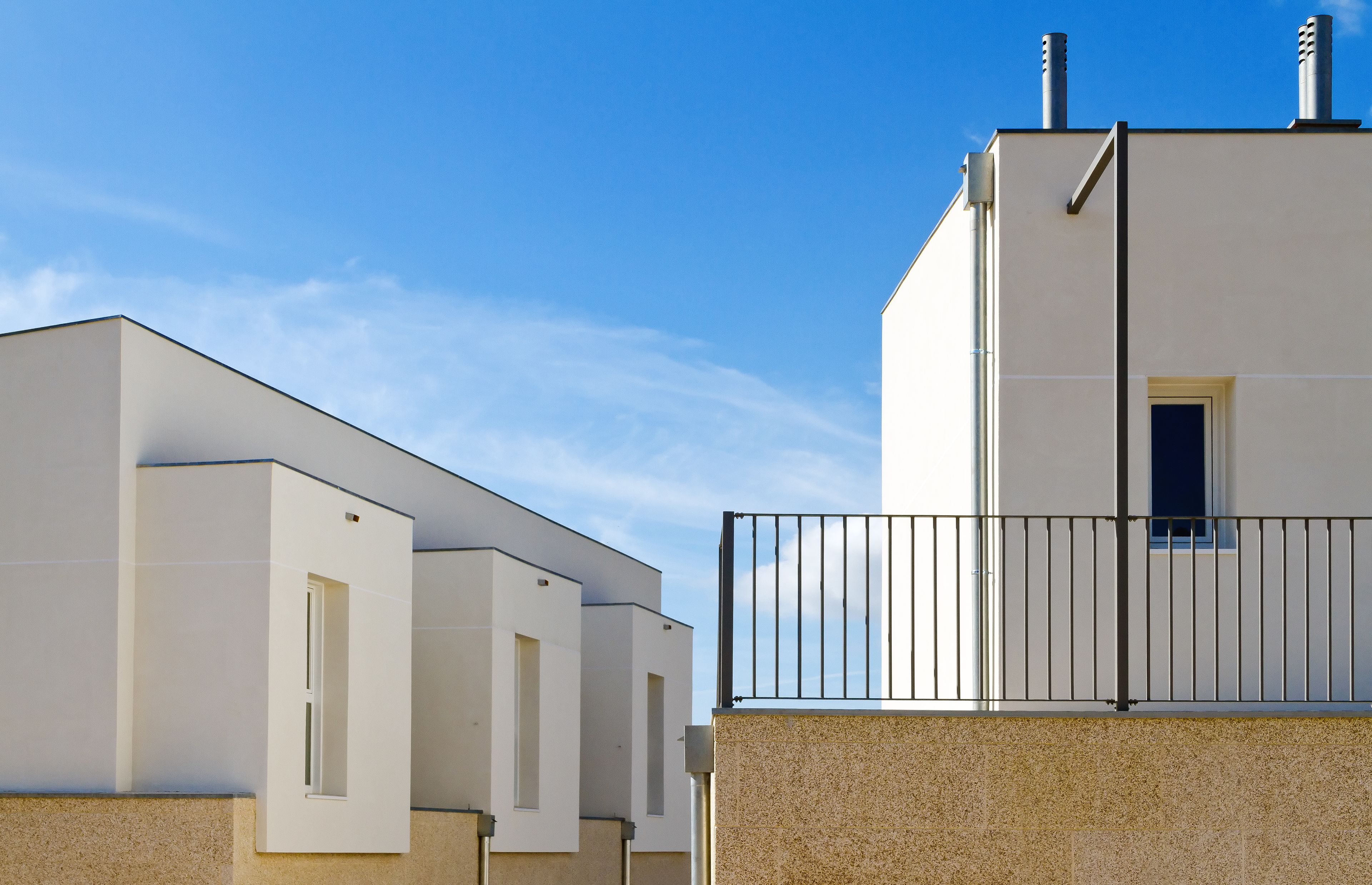 A modern building with a flat roof, a small window, and a metal railing.