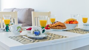 Una mesa de desayuno con un croissant, un bol de fruta y vasos de zumo de naranja.