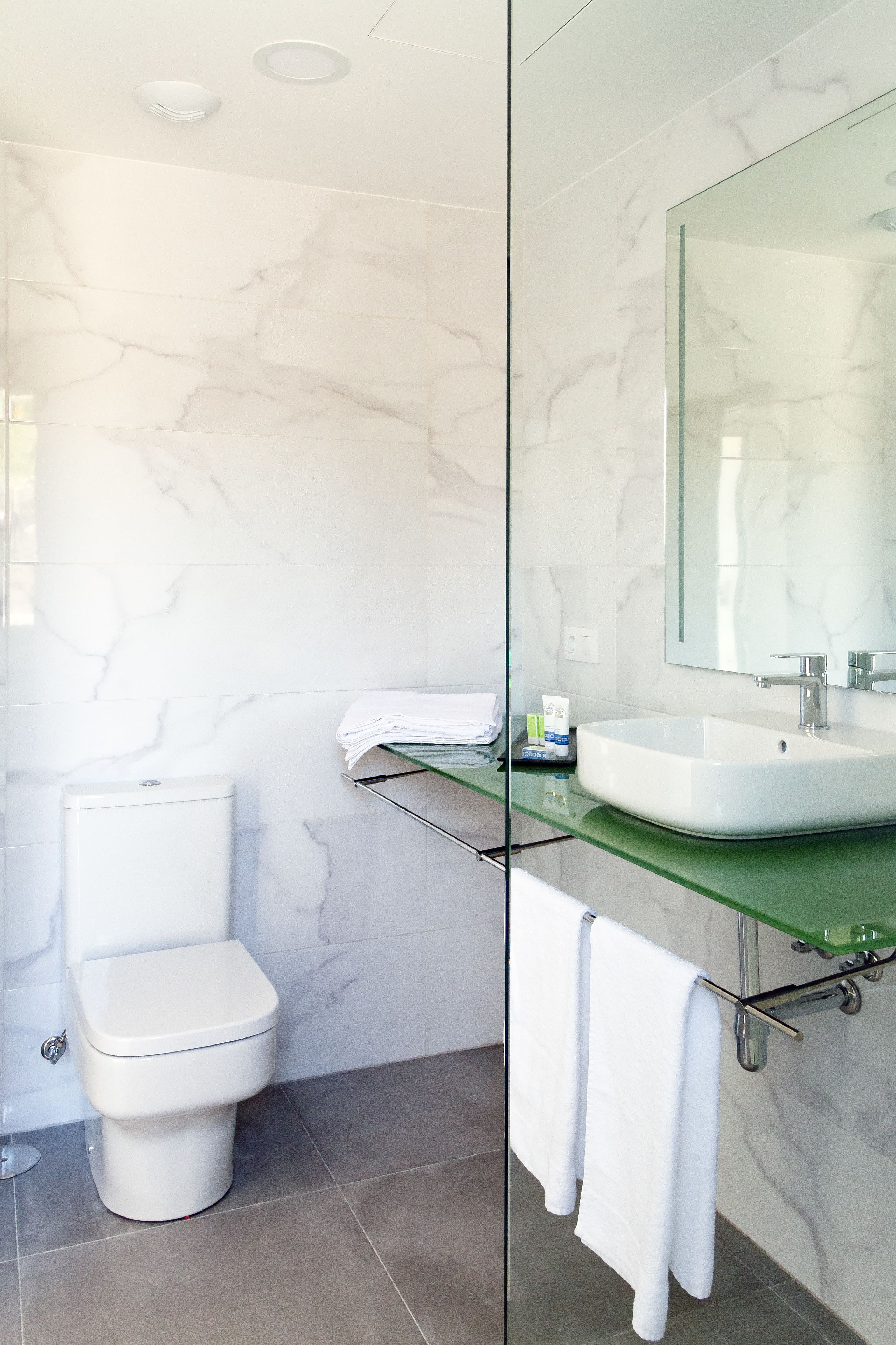 A modern bathroom with a white toilet, a glass shower enclosure, and a marble-tiled wall.