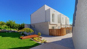Una casa moderna de dos pisos con techo plano, cerca de madera y un césped bien cuidado.