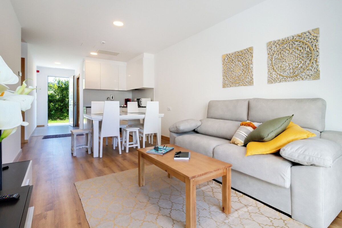 A modern living room with a grey sofa, a wooden coffee table, and a dining area with white chairs and a white table.