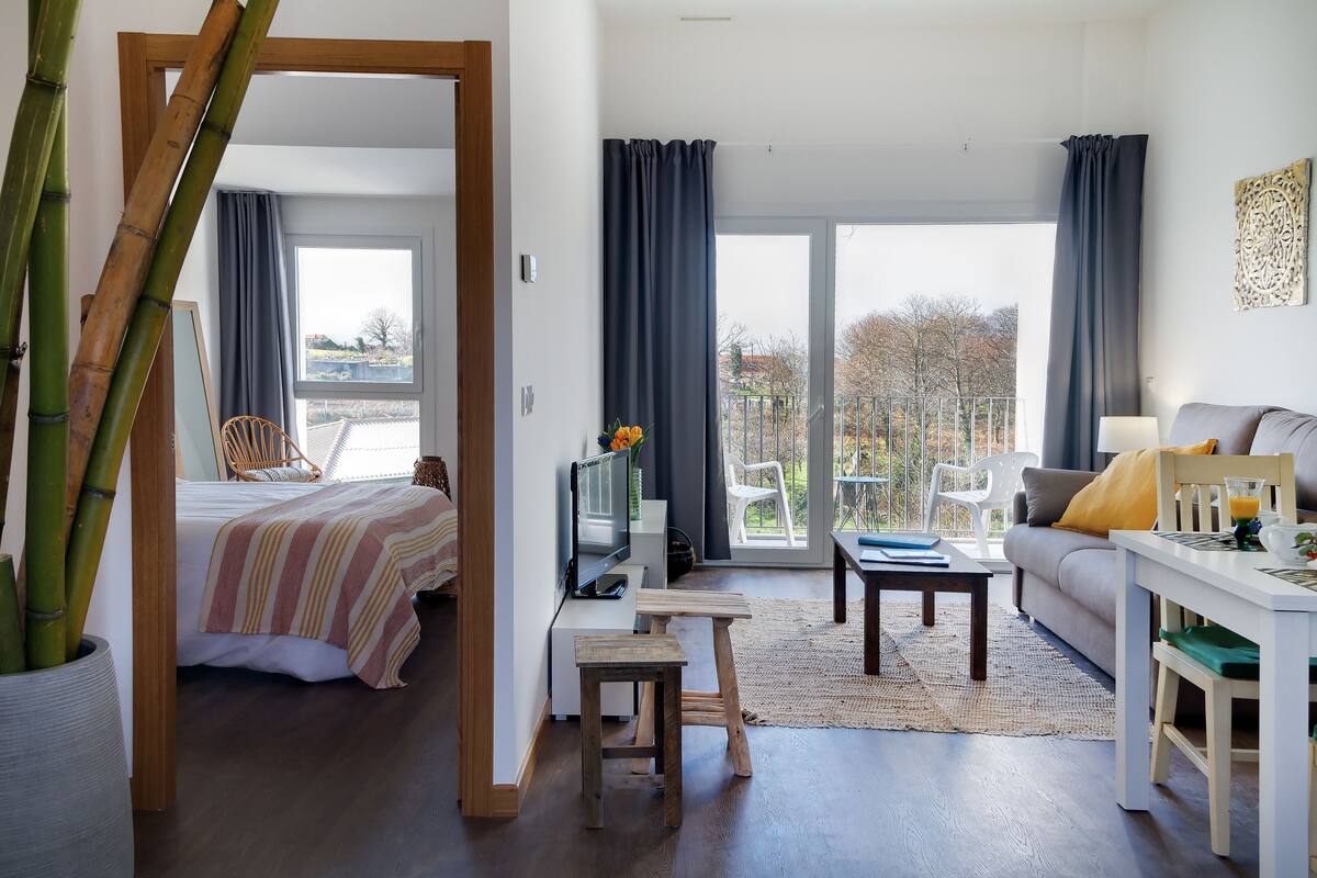 Una sala de estar moderna con una cama, un sofá, un televisor y un balcón con cortinas.
