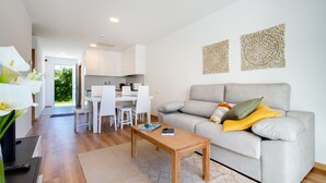 Una sala de estar moderna con un sofá gris, una mesa de centro de madera y un comedor con sillas y mesa blancos.