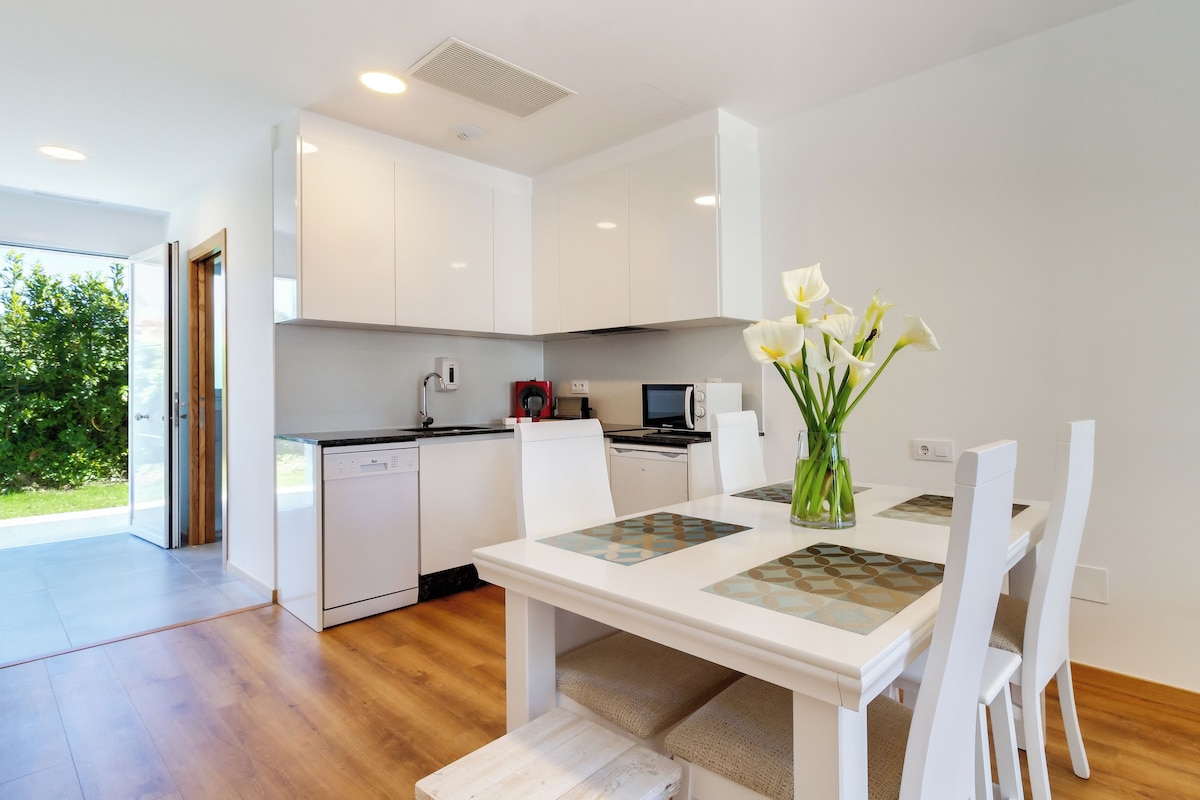 A modern kitchen with white cabinets, a built-in microwave, and a dishwasher. There is a dining table with chairs and a vase of flowers.