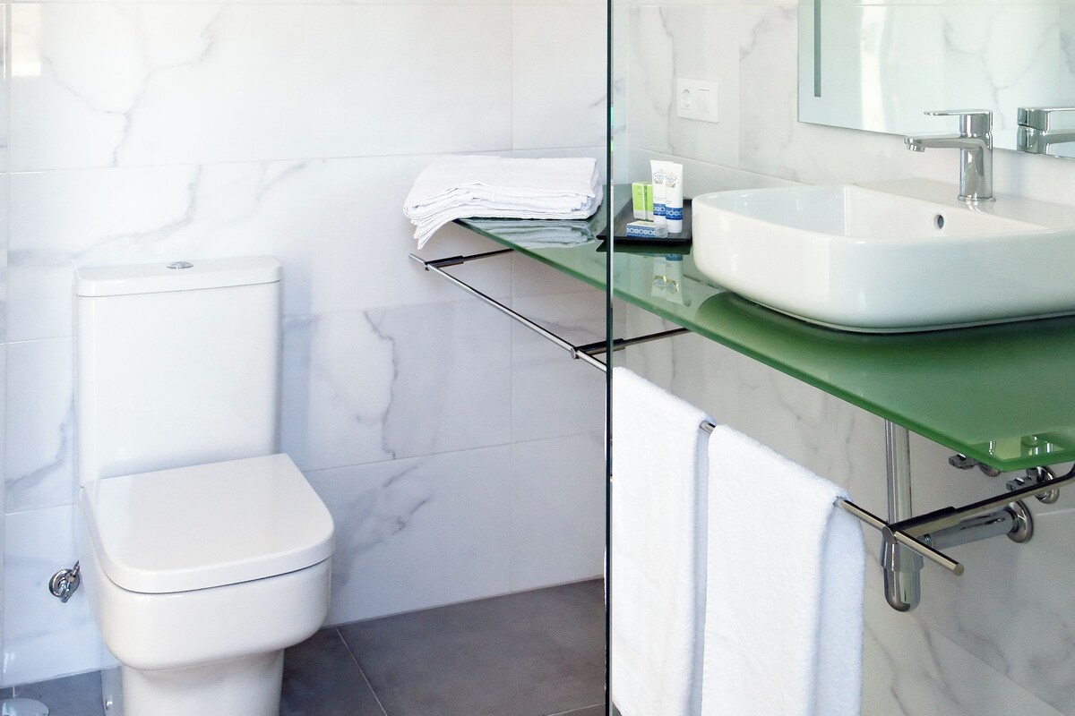 Une salle de bain moderne avec des toilettes blanches, une douche en verre et un mur recouvert de carreaux de marbre.