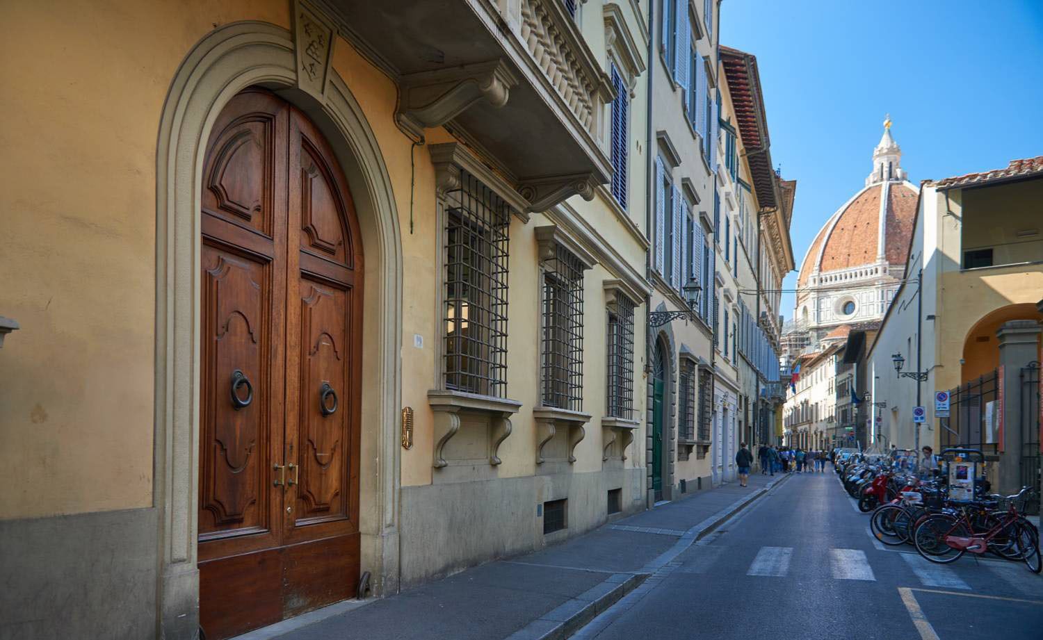 A narrow street lined with historic buildings, featuring a prominent wooden door and a domed building in the background.