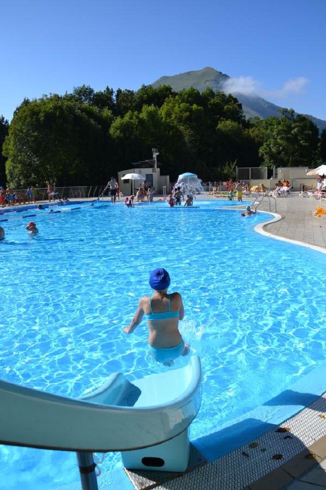 Una piscina con gente, una torre de socorristas y una montaña al fondo.