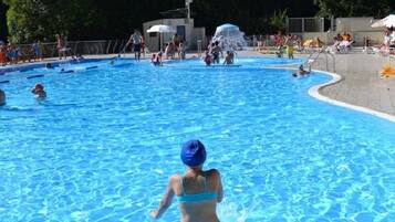 Une piscine avec des personnes dans l’eau, un poste de surveillance pour les sauveteurs et une montagne en arrière-plan.