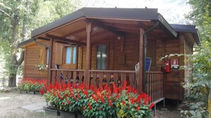 A wooden cabin with a porch, surrounded by red flowers, and a fire extinguisher visible. - Campeggio Valle Gesso (Entracque)
