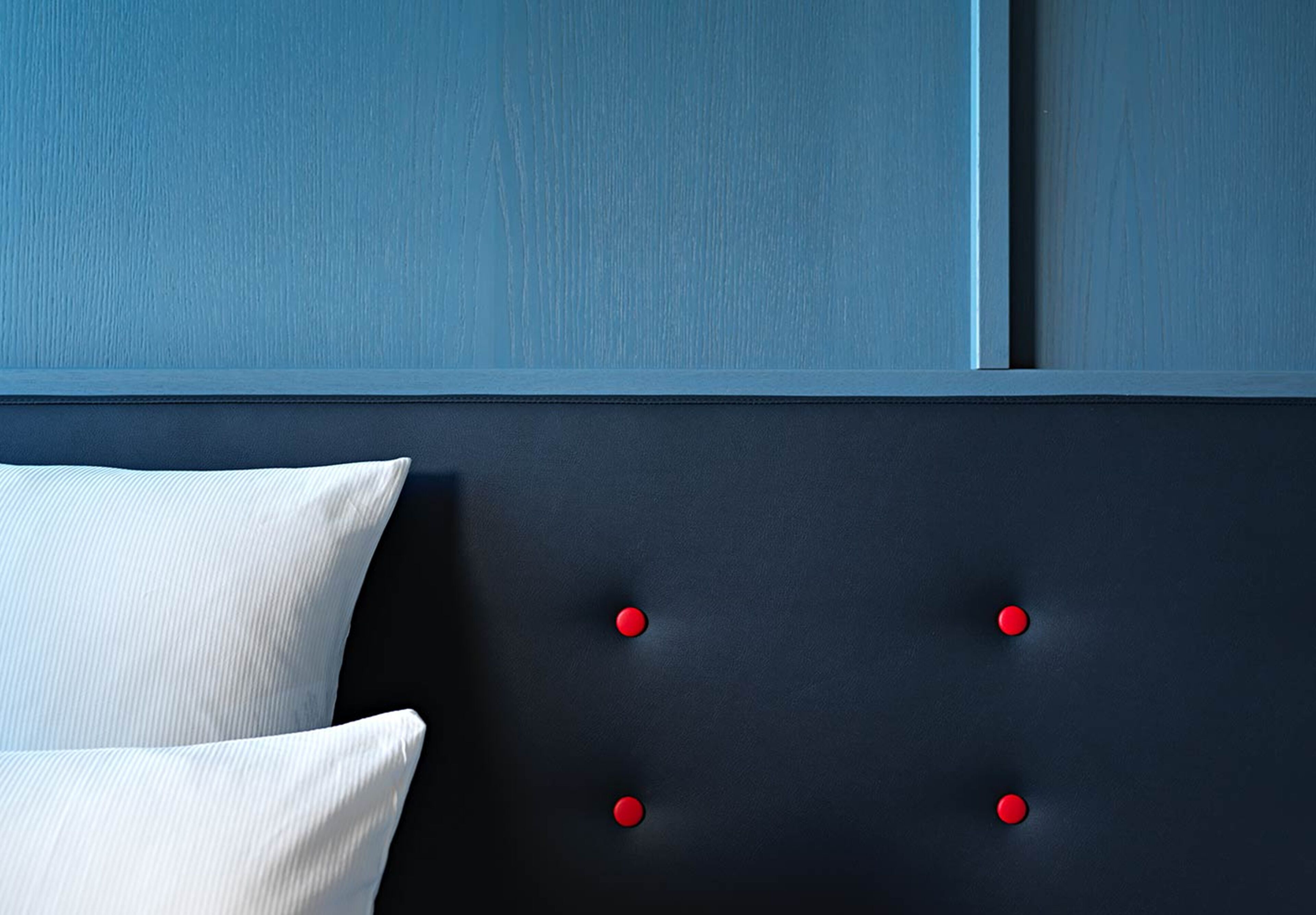 Een slaapkamer met een donker hoofdeinde en rode knopen, een wit kussen, en een blauwe muur.