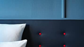 Een slaapkamer met een donker hoofdeinde en rode knopen, een wit kussen, en een blauwe muur.
