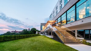Een modern gebouw met een glazen gevel, een trap die naar een hoger gelegen niveau leidt en een verzorgd gazon ervoor.