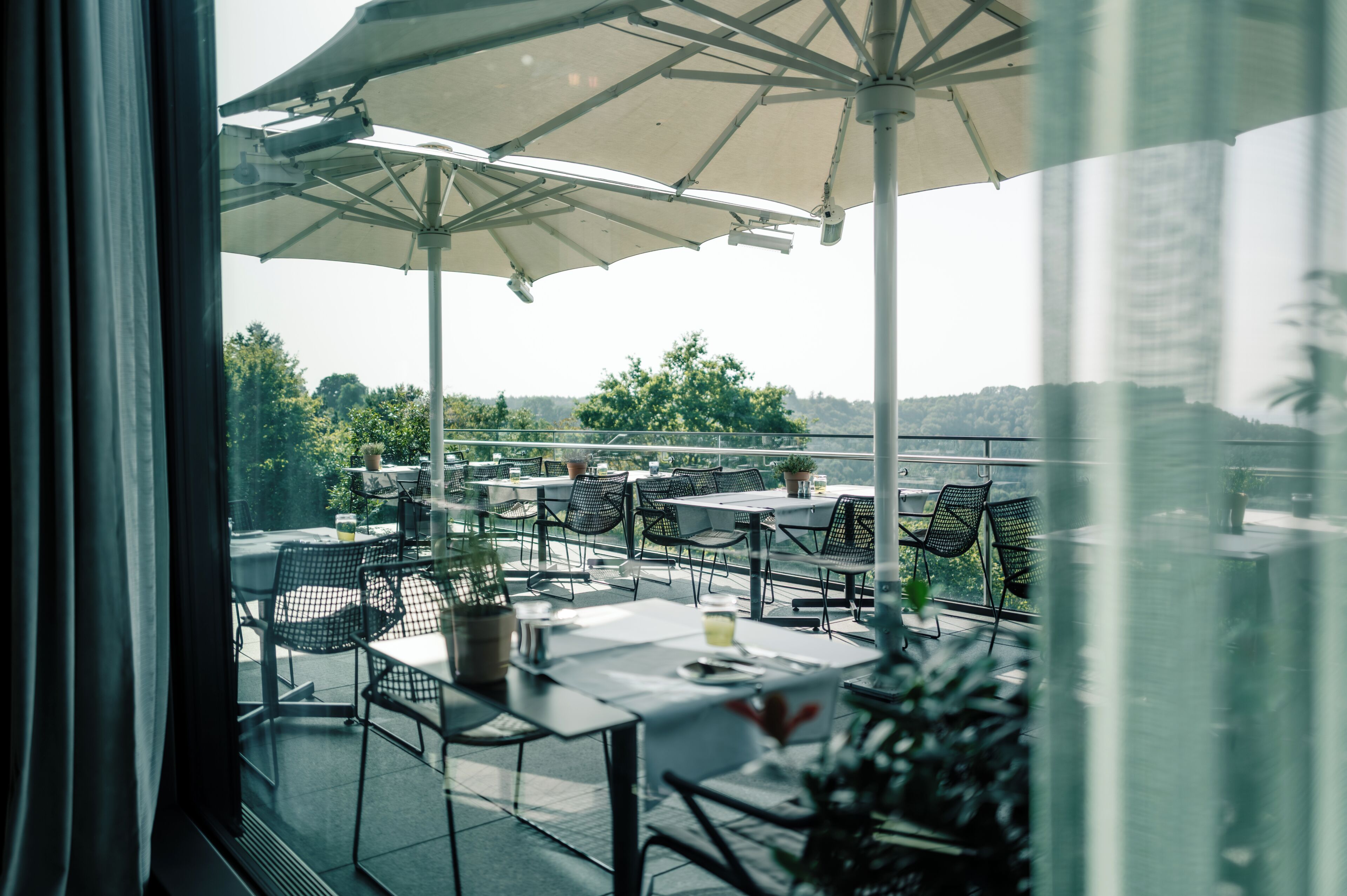 Ein Terrassenbereich im Freien mit Tischen, Stühlen, Sonnenschirmen und Topfpflanzen.