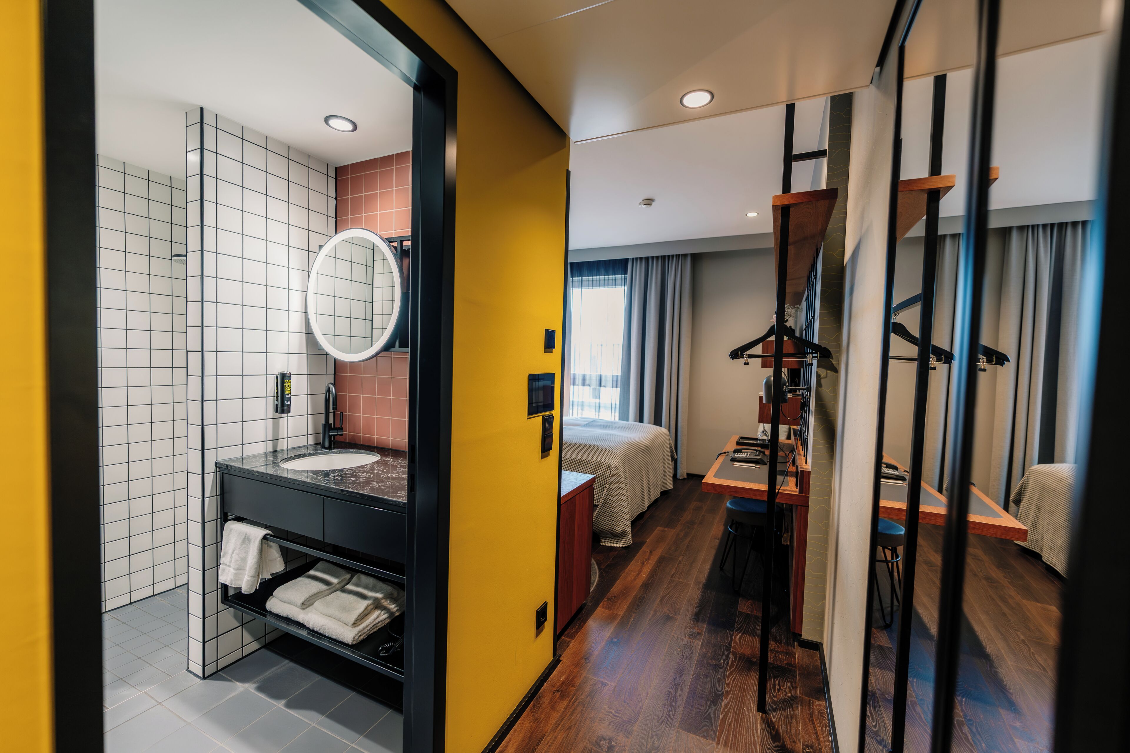 Ein modernes Hotelzimmer mit Bad, Bett, Schreibtisch und Kleiderschrank.