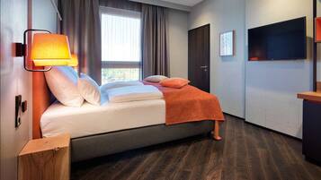 A modern hotel room with a bed, a nightstand, a TV, and a window with curtains.