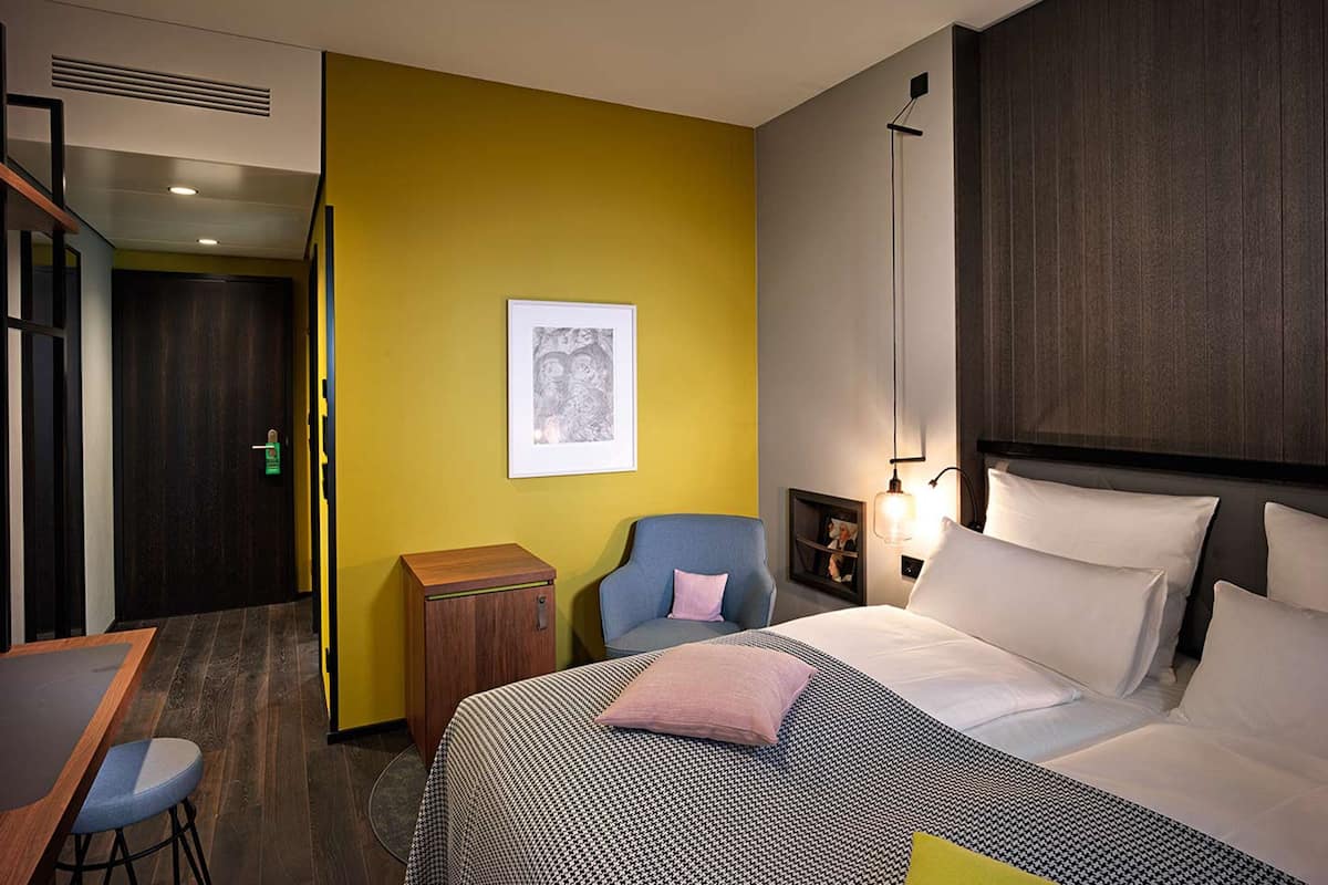 A hotel room with a bed, a desk, a chair, and a small cabinet.