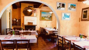 Un restaurant amb diverses taules preparades per dinar, cadires de fusta i una llar de foc amb un cartell a dalt.