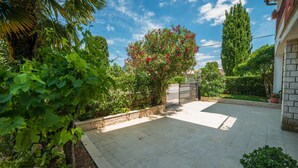 Une cour dallée, entourée d’une végétation luxuriante et de diverses espèces de plantes.