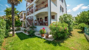Un immeuble à plusieurs étages doté de balcons, de plantes en pot et d’une pelouse bien entretenue.