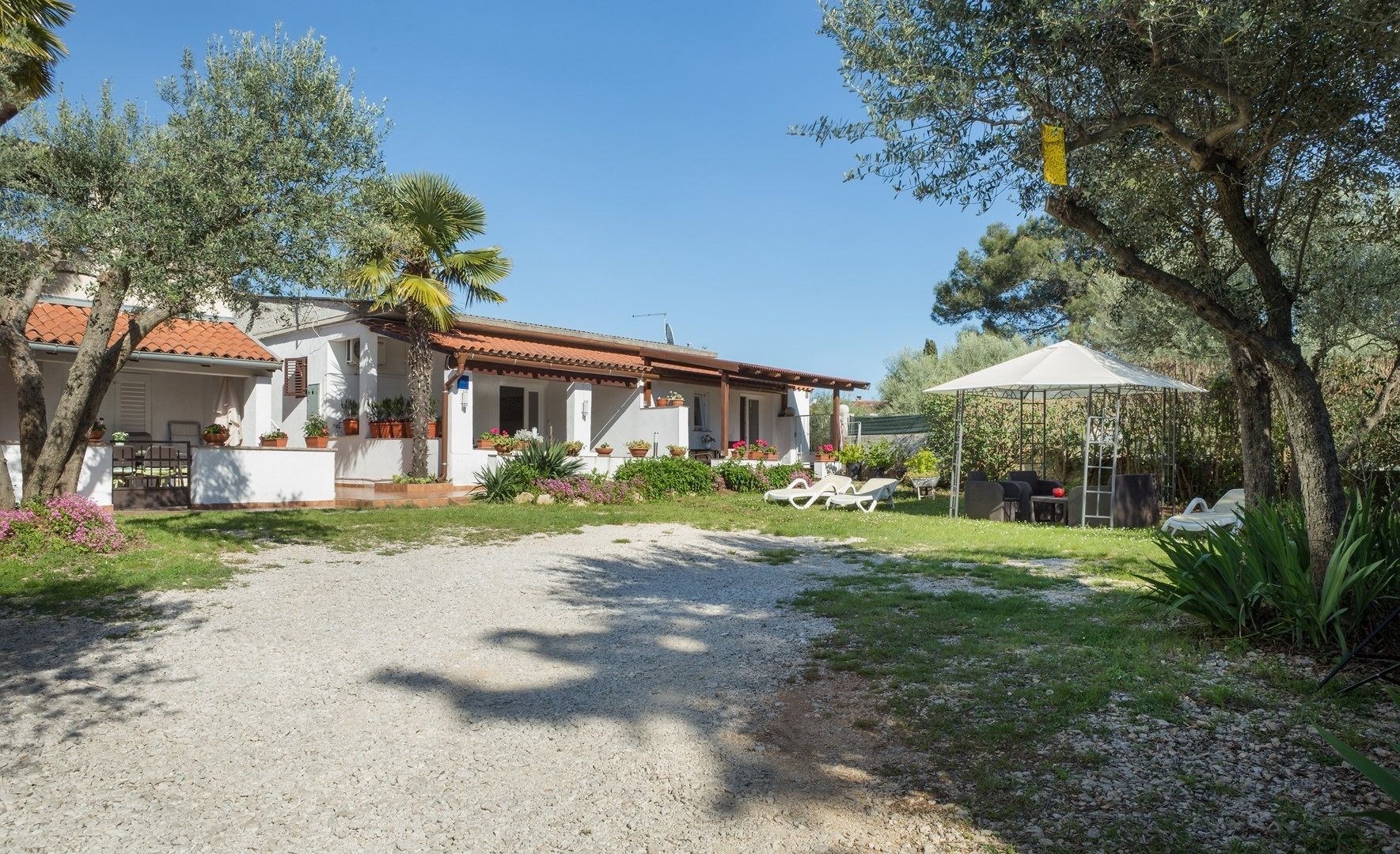 Une maison avec une allée en gravier, un espace extérieur aménagé pour s’asseoir et une zone couverte.