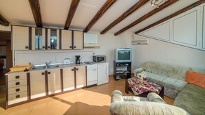 Cocina compacta con vigas de madera, zona de comedor con sofá y televisor.
