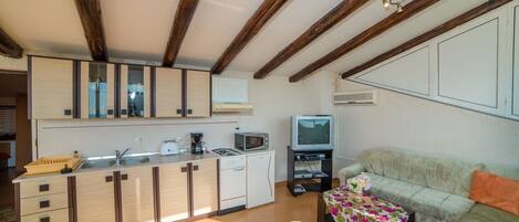 A compact kitchen with wooden beams, a dining area with a sofa, and a television.