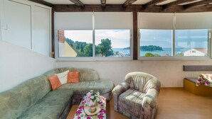 Habitación con un ventanal grande que ofrece vistas al agua y vegetación. Cuenta con un sofá verde y un sillón estampado.