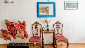 Habitación con dos sillas de madera adornada con cojines rojos, una mesita con un reloj y un florero, y un espejo con marco azul en la pared.