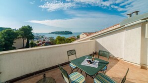 Una terraza con mesa y sillas, con vistas a la costa, edificios y árboles.