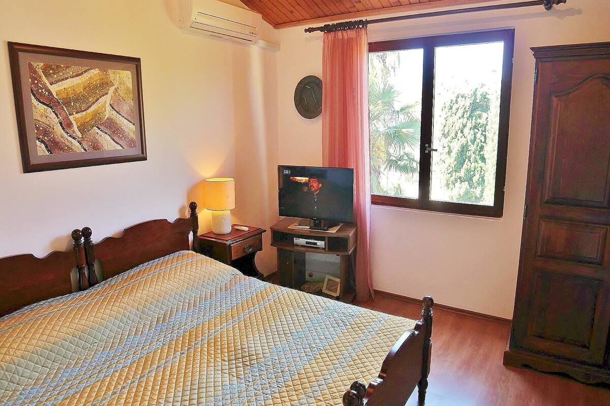A bedroom with a bed, a television, a clock, and a window with curtains.