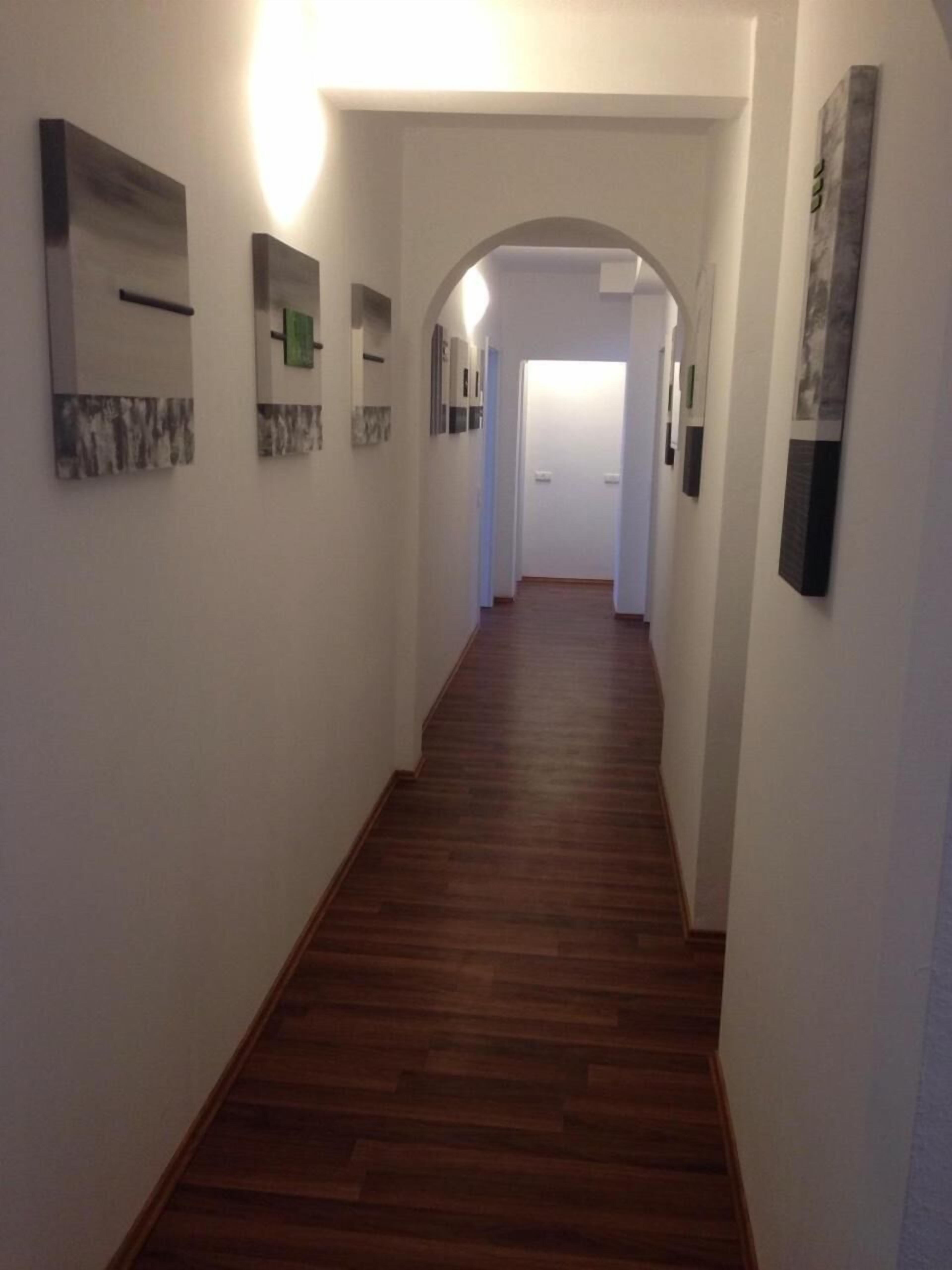 Un couloir doté d’un plancher en bois, de murs blancs et d’œuvres d’art encadrées.