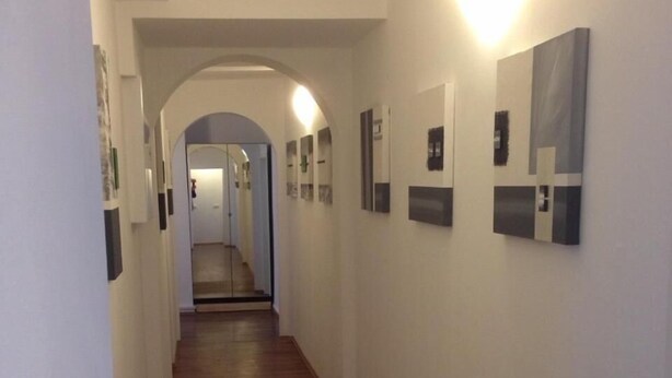 A hallway with wooden flooring, white walls, and a series of framed pictures. - Porschepension (Wolfsburg)