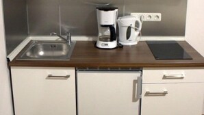 A compact kitchen with white cabinets, a built-in sink, a coffee maker, and a small refrigerator. - Porschepension (Wolfsburg)