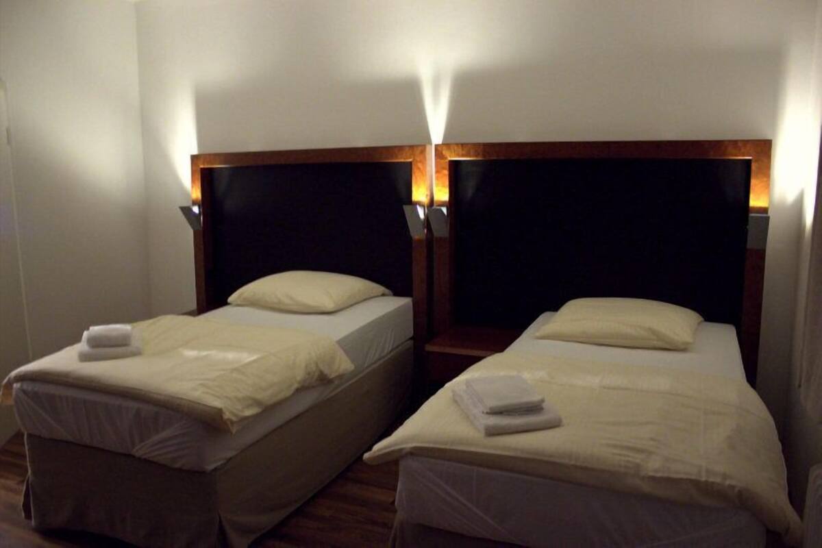 Two single beds with wooden headboards and white linens, in a room with white walls and a wooden floor.